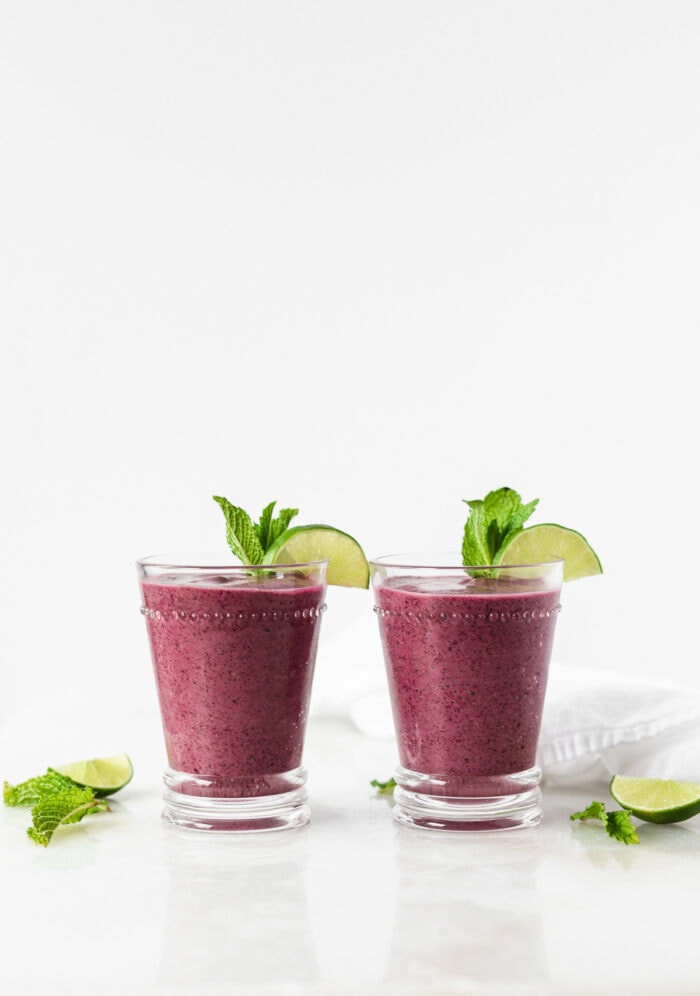 two blueberry mojito smoothies in glasses garnished with lime wedges and mint.