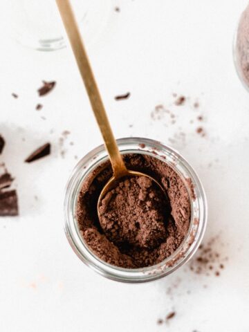 overhead view of dark chocolate hot cocoa mix in a jar with a gold spoon in it.