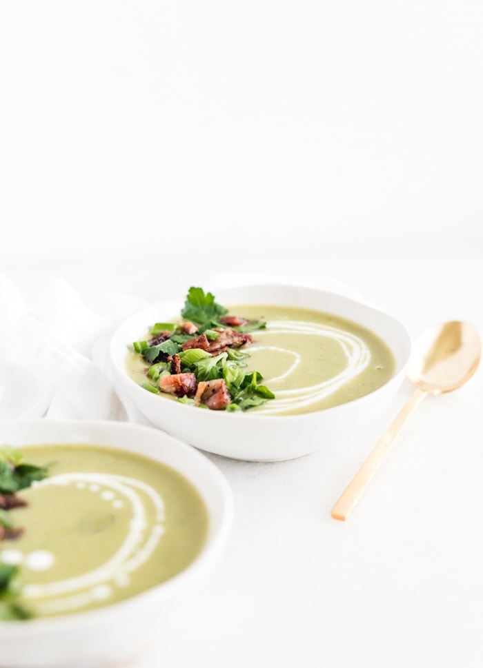 two bowls of creamy potato split pea soup with a gold spoon and a white napkin.