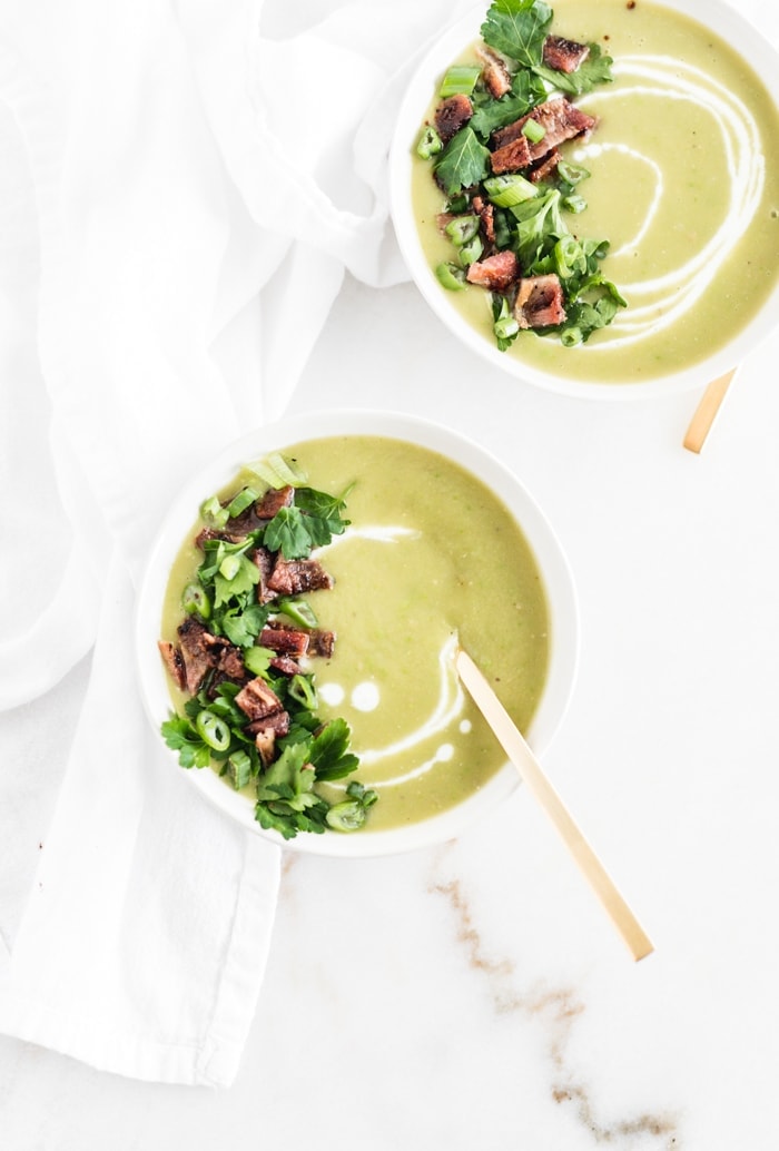 overhead view of two bowls of creamy potato split pea soup with gold spoons and a white napkin.