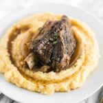 closeup of slow cooker balsamic braised short ribs on top of polenta on a white plate.