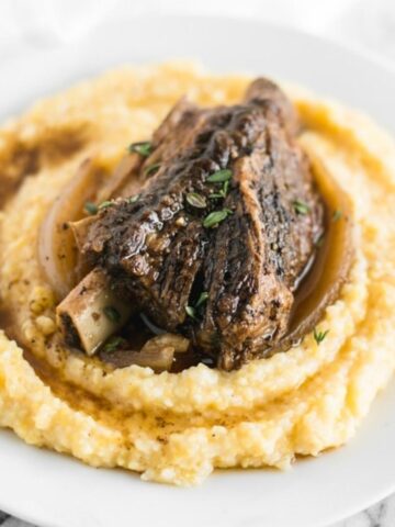 closeup of slow cooker balsamic braised short ribs on top of polenta on a white plate.