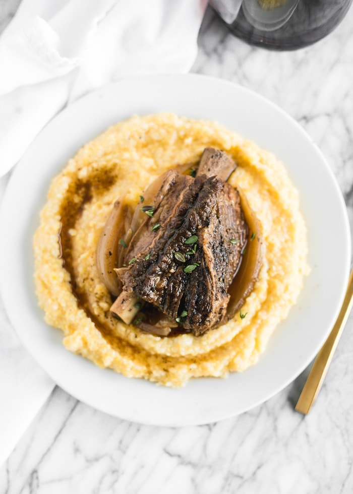 overhead view of slow cooker balsamic braised short ribs on polenta on a white plate.