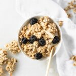 overhead view of coconut tahini granola and blackberries in a bowl with a gold spoon.