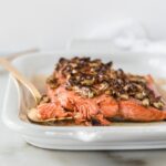 honey pecan salmon filet flaked on the corner with a gold fork beside it on a white platter.