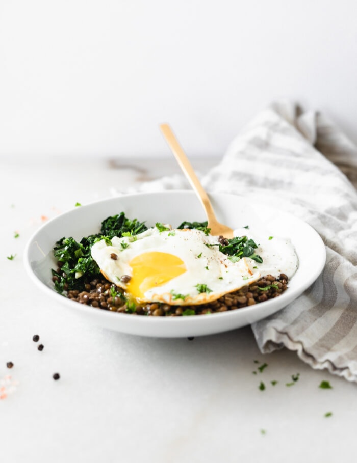 kale lentil breakfast bowl with a runny fried egg with a grey and white napkin next to it.