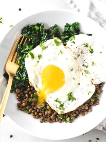 overhead view of kale, lentils, yogurt and a fried egg with a gold fork in a white bowl.