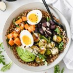 overhead view of roasted vegetable grain bowl with a soft boiled egg and tahini sauce.