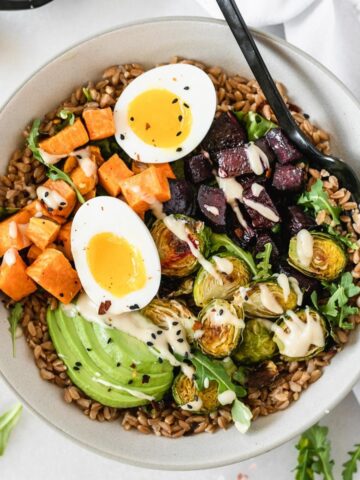 overhead view of roasted vegetable grain bowl with a soft boiled egg and tahini sauce.