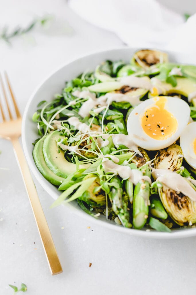 closeup of soft boiled egg and sliced avocado on top of a spring greens grain bowl.