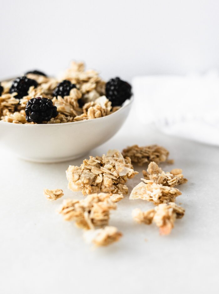 chunks of tahini coconut granola next to a white bowl of granola and berries.