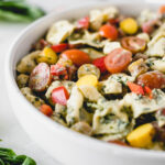 closeup of creamy tortellini pesto pasta salad with tomatoes and carrots in a bowl.
