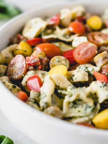 closeup of creamy tortellini pesto pasta salad with tomatoes and carrots in a bowl.