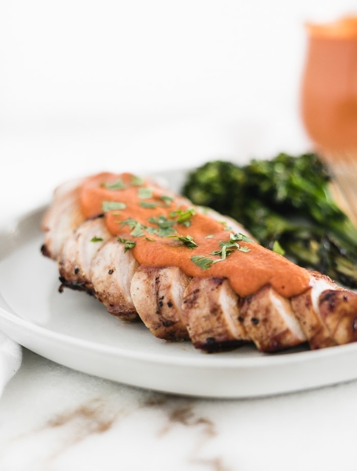 grilled sliced chicken breast topped with romesco sauce and sprinkled with parsley.