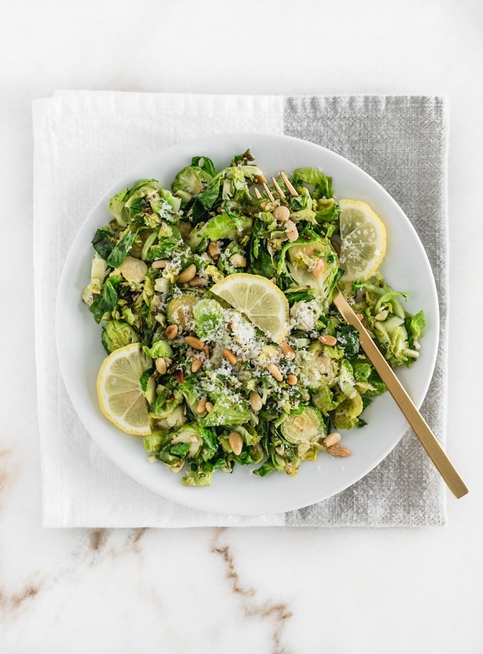 Lemon Parmesan Shaved Brussels Sprouts on a white plate with a gold fork on top of a grey and white napkin.