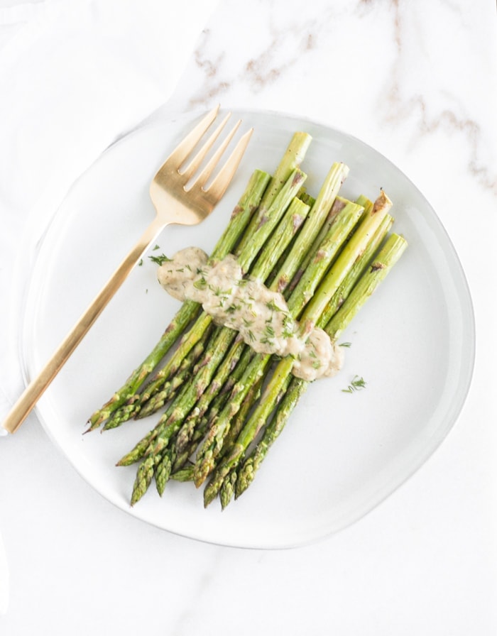overhead view of roasted asparagus with dijon dill sauce on a white plate with a gold fork.