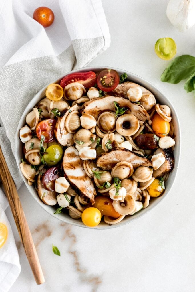 Chicken Caprese pasta salad in a big bowl with vinaigrette poured over it.