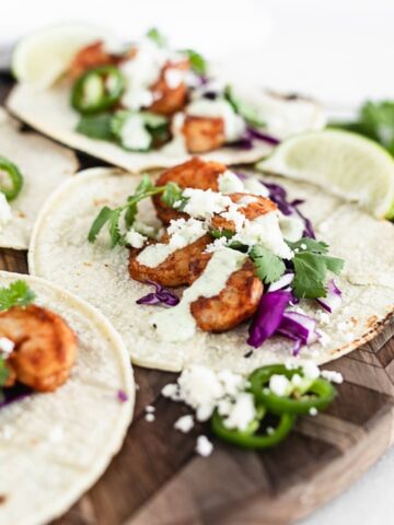 shrimp taco on a wooden cutting board with jalapeno lime cream sauce, cotija, purple cabbage and cilantro.