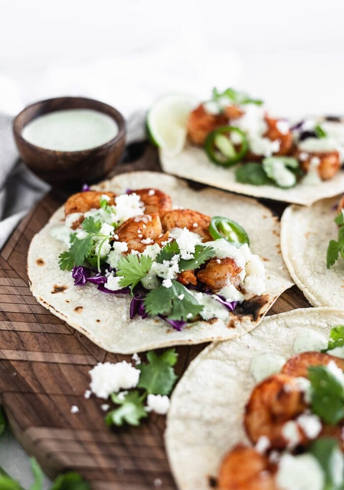 A close up of a easy chipotle shrimp taco with cilantro jalapeño sauce on a wooden tray.