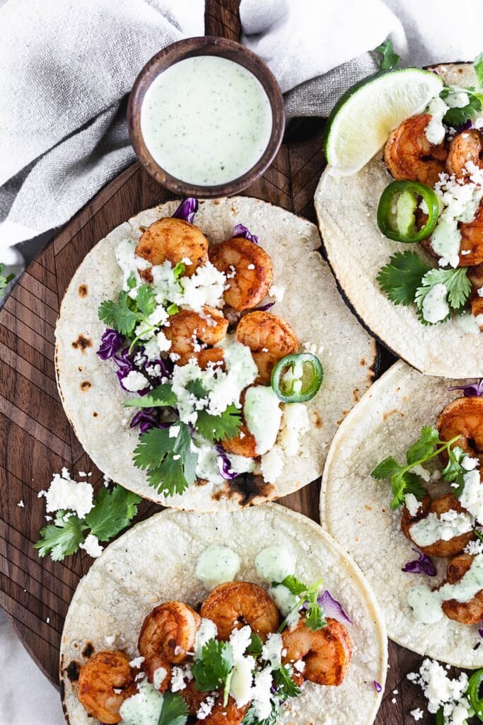 Easy chipotle shrimp tacos with cilantro jalapeño sauce on a wooden serving board.