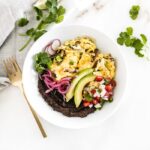 overhead view of healthy migas breakfast bowl in a white bowl with a gold fork and a napkin next to it.