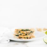 Spinach mushroom hummus quesadilla triangles stacked on a white plate.