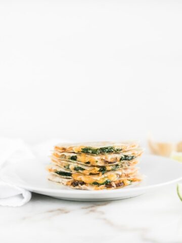 Spinach mushroom hummus quesadilla triangles stacked on a white plate.