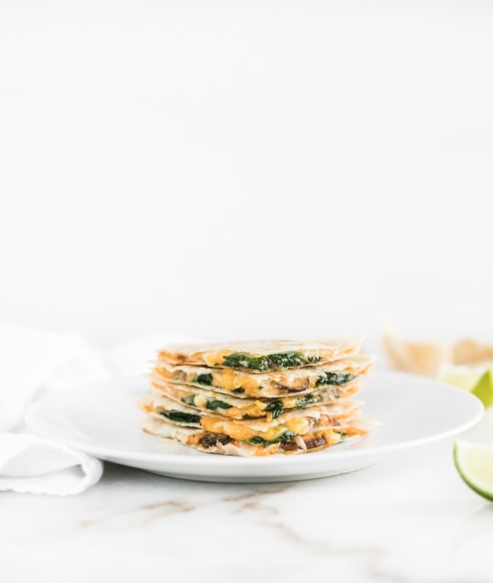 Spinach Mushroom Hummus Quesadilla triangles stacked on a white plate.