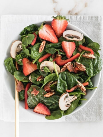 overhead view of La Madeleine Copycat Strawberry Spinach Salad in a white bowl on a grey and white napkin.