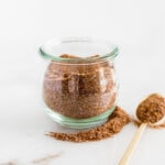 BBQ spice rub in a glass jar with a gold spoon beside it.