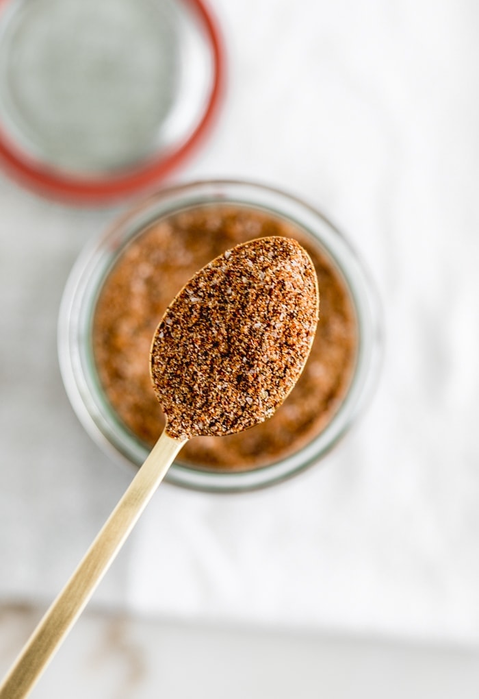 Overhead view of a gold spoon lifting a spoonful of homemade BBQ spice rub out of a jar.