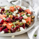 closeup of watermelon beet salad with goat cheese and walnuts in a grey plate.