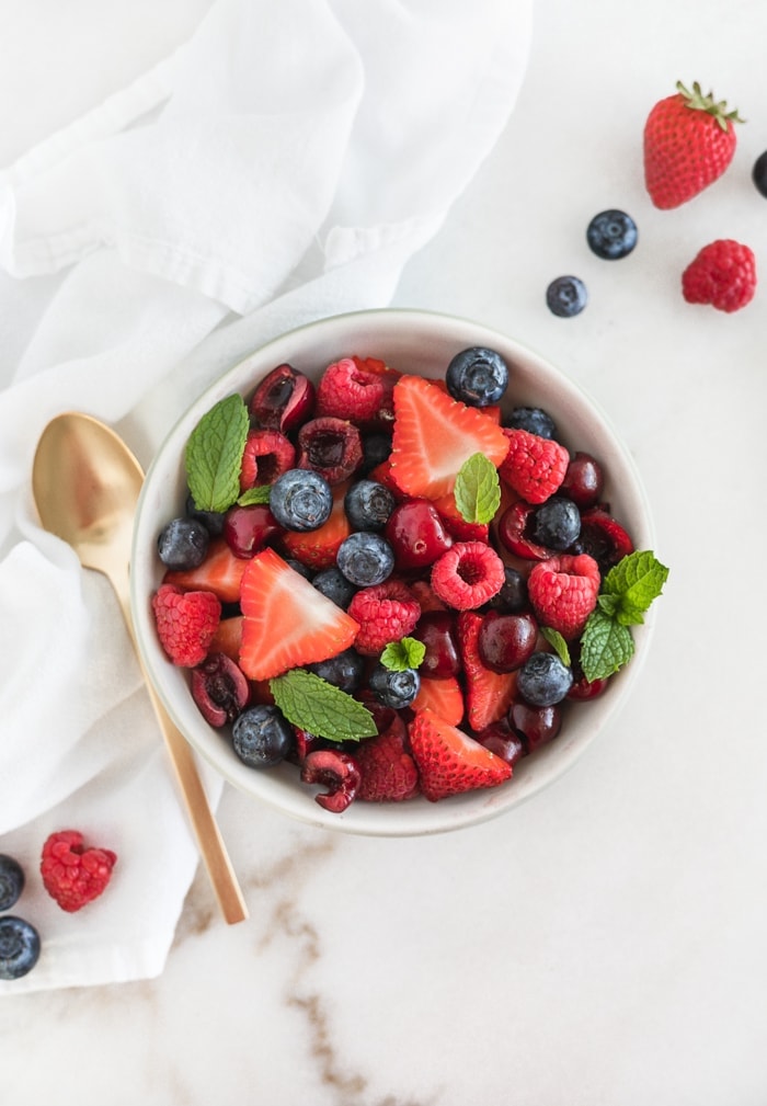 overhead view of red white and blue fruit salad in a bowl with a gold spoon beside it.