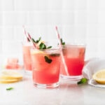 three glasses of watermelon mint lemonade with pink striped straws surrounded by lemon slices and mint leaves.