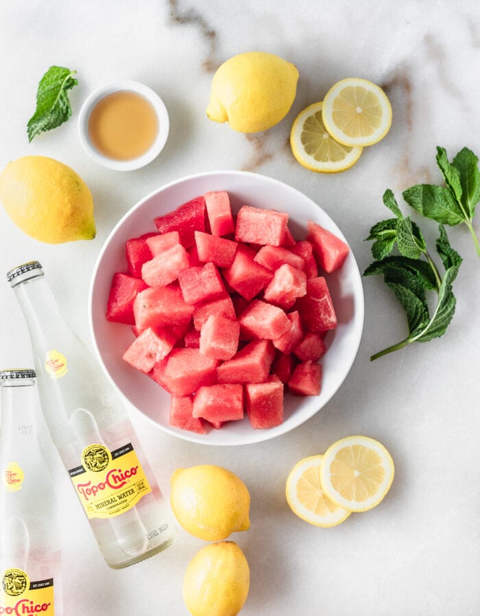 overhead view of ingredients needed to make sparkling watermelon mint lemonade on a white background.