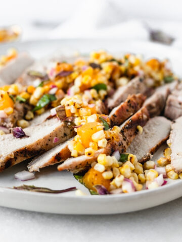 sliced pork chops topped with grilled apricot and corn salsa on a plate.