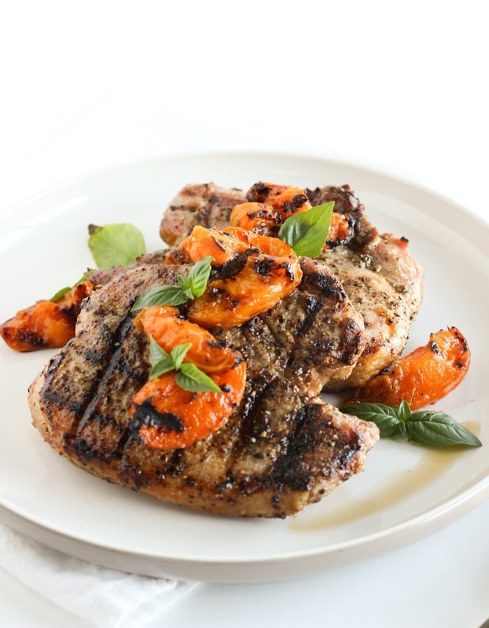 grilled pork chops with grilled apricots and basil on top on a white plate.