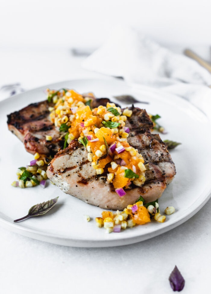 grilled pork chops topped with grilled apricot corn salsa on a grey plate.