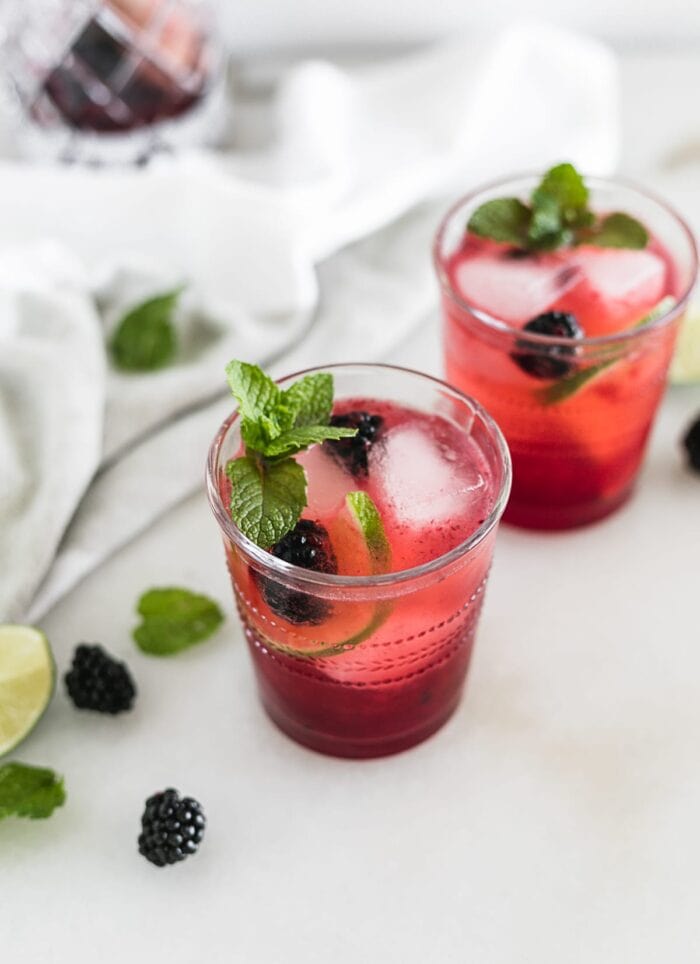 blackberry bourbon smash cocktail in a glass with lime slices and blackberries, with another cocktail in the background.