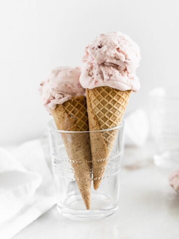 two strawberry ice cream cones in a glass cup n front of a white background.