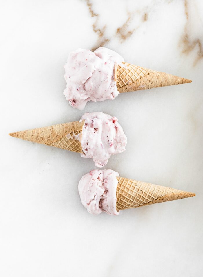 overhead view of three strawberry ice cream cones laying flat on a white marble surface.