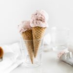 two strawberry ice cream cones in a glass cup n front of a white background.