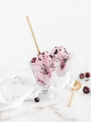 Cherry chocolate chunk frozen yogurt in clear dishes with gold spoons, fresh cherries, and a white napkin next to it.