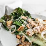 Closeup view of grilled Caesar salad with shrimp on a white plate with a gray and white napkin next to it.
