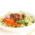 Zucchini noodle poke bowl in a white bowl with a gold fork next to it.