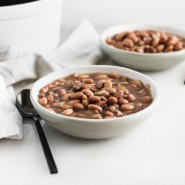 pinto beans a grey bowl with a black spoon beside it.