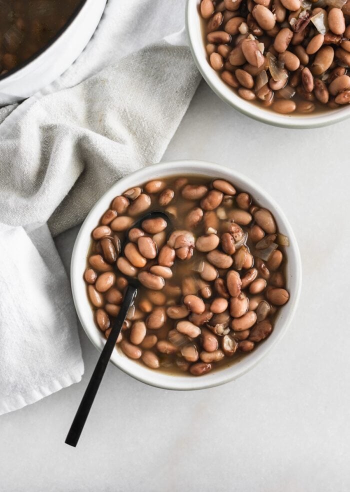 overhead view of pinto beans in a grey bowl with a black spoon in it.