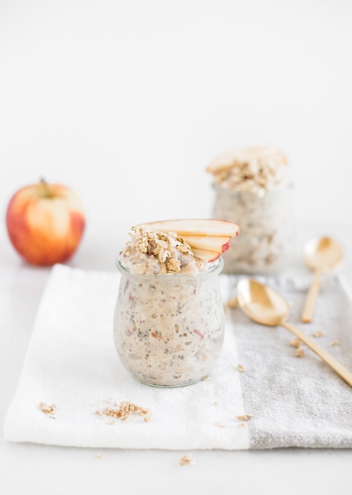 apple pie overnight oats in a glass jar with apple slices on top and another jar of oats in the background.