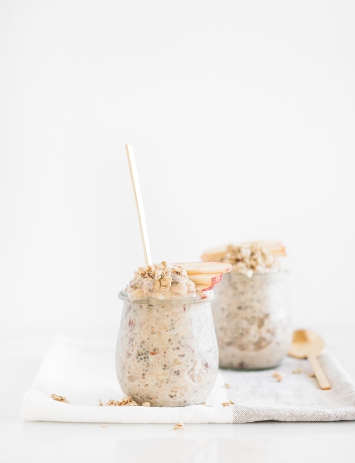 glass jar of apple pie overnight oats with apple slices on top and a gold spoon in it.