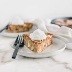slice of healthy apple cake topped with whipped cream on a grey plate with a black fork.